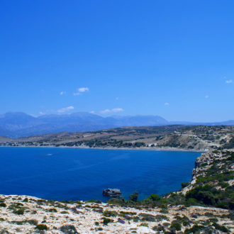 Rocky coastal bay with deep blue sea, distant mountains, and a clear sky in South Crete