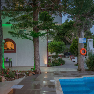 Courtyard pool area at Houmeli Apartments with trees, tiled walkway, and white buildings in Kalamaki Crete