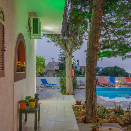 Courtyard pool area with lounge chairs, trees, and potted plants at Houmeli Apartments in Kalamaki Crete