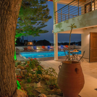 Nighttime courtyard at Houmeli Apartments with a pool, lounge chairs, and a terrace beside the building