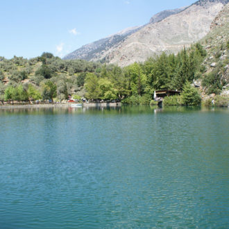 Mountain lake with calm water, trees along the shore, and rocky slopes under a clear sky