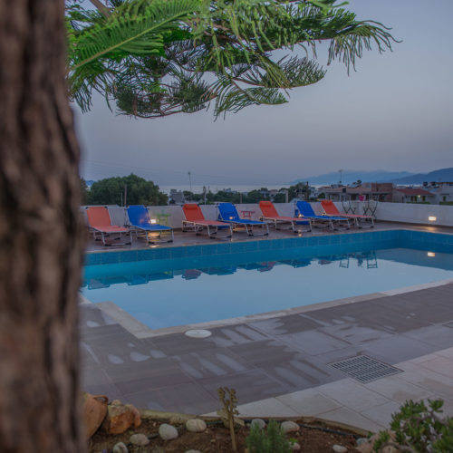 Outdoor swimming pool with colorful sun loungers at Houmeli Apartments in Kalamaki Crete at dusk