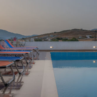 Sun loungers line the pool terrace beside calm water, with mountain views at Houmeli Apartments in Kalamaki Crete
