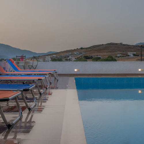 Sun loungers line the pool terrace beside calm water, with mountain views at Houmeli Apartments in Kalamaki Crete