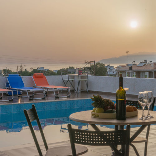 Poolside terrace with sun loungers, a table set with fruit and wine, and a sunset view over the sea