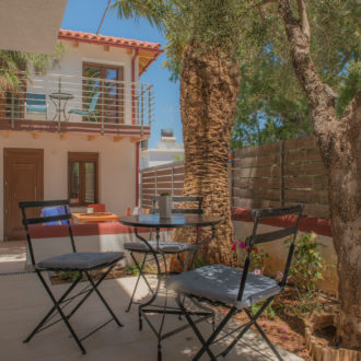 Shaded outdoor seating area with tables and chairs beside a two-story apartment building and palm trees