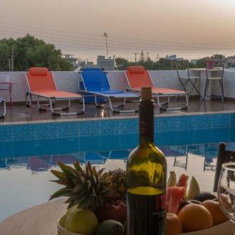 Poolside terrace with sun loungers, table setting, and sunset sea view at Houmeli Apartments