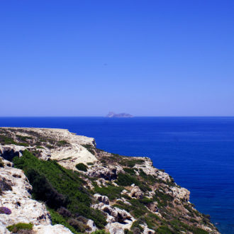 Rocky coastal cliffs above deep blue sea with a small island on the horizon