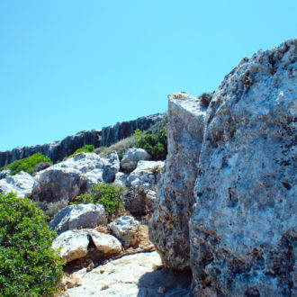 Rocky coastal cliffs and boulders beneath a clear blue sky in South Crete