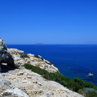 Rocky coastal cliff overlooking a deep blue sea with a small island on the horizon