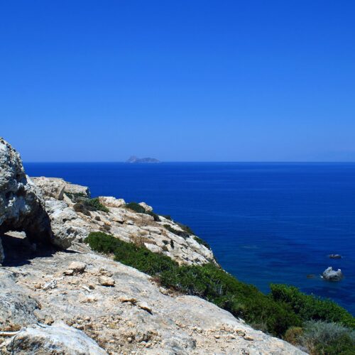 Rocky coastal cliff overlooking a deep blue sea with a small island on the horizon