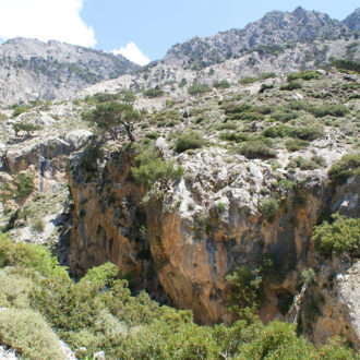 Rocky mountain gorge with sparse shrubs and a bright blue sky in South Crete