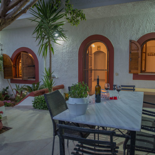 Shaded patio with dining table, chairs, potted plants, and arched windows at Skinos apartment