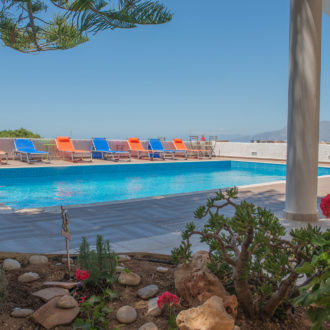 Outdoor swimming pool with colorful sun loungers, potted plants, and mountain views at Houmeli Apartments