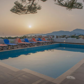 Outdoor pool terrace with sun loungers, mountain views, and a calm sunset sky at Houmeli Apartments in Kalamaki Crete