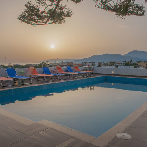 Outdoor pool terrace with sun loungers, mountain views, and a calm sunset sky at Houmeli Apartments in Kalamaki Crete