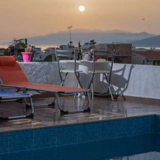 Pool terrace with lounge chairs, a small table, and mountain views at sunset in Kalamaki Crete
