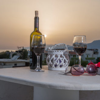 Wine glasses and a bottle on a terrace table at sunset, with sunglasses and a lantern in the foreground