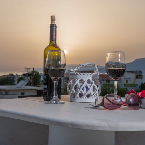 Wine glasses and a bottle on a terrace table at sunset, with sunglasses and a lantern in the foreground