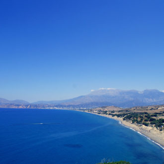Wide coastal view of Kommos beach with blue sea, sandy shore, and distant mountains