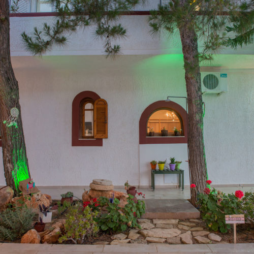 Landscaped exterior of a white apartment building with arched windows, trees, and potted flowers